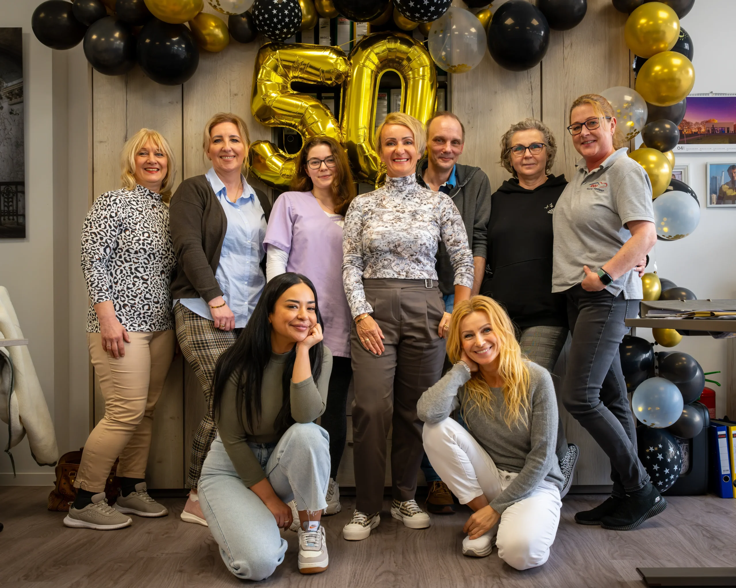 Teamfoto mit goldener 50 beim Jubiläumsevent Neun Personen des Teams posieren vor goldener 50 aus Luftballons bei einem feierlichen Jubiläumsevent im Büro